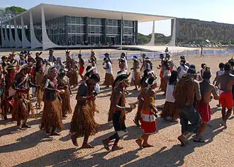 People wearing traditional Indigenous garments are forming a circle while walking outdoors