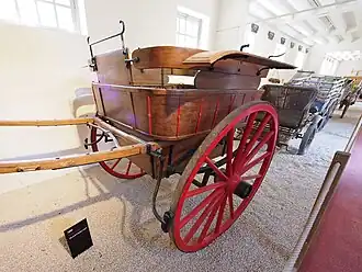 This image shows the typical dropped axle, elliptical springs, iron-clad wheels, and fenders. This large cart even has brakes.