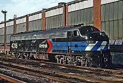 A black diesel locomotive with the Amtrak "pointless arrow" logo on the side. The blue stripes of the logo wrap around the front, where they are checked with white.