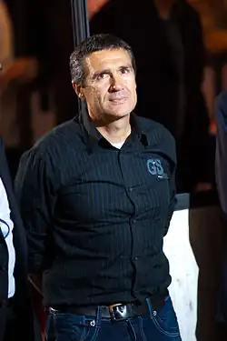 A man wearing a navy pinstriped button-up with his arms behind his back.