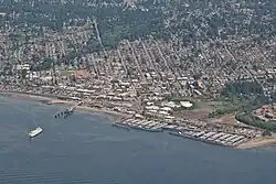 An aerial picture of Downtown Edmonds, showing a city laid out in a grid of streets and buildings. The water takes up the bottom half of the picture, with a ferry approaching the dock.