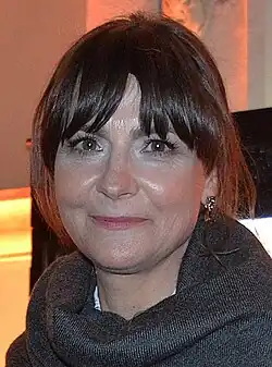 middle-aged white woman with dark hair wearing dark gray top, smiling at camera