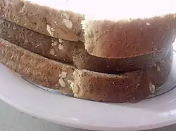 An image of a toast sandwich, shot from the side, consisting of two thin-cut slices of bread and one thick-cut slice.