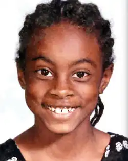 A young girl with dark brown skin and braided black hair, smiling