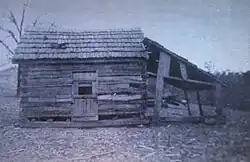 A log cabin with some logs missing and a lean-to attached to its side