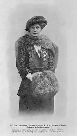 Three-quarter length portrait photograph of a lady wearing an Edwardian-style dress and hat with furs