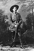 Black-and-white photo of Buffalo Bill in front of a forest backdrop, holding a Winchester