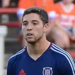 A soccer player is standing. The photo shows him from the chest up.