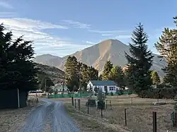 Small houses backed by pine trees with bare mountains and blue sky in the distance