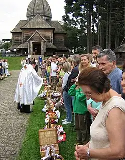 A line of people stand outside a church greeted by a priest while a woman bows her head
