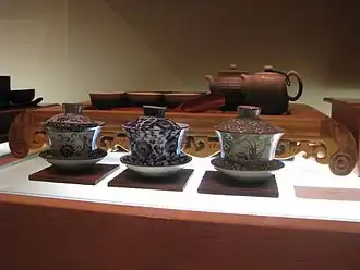 Three gaiwan in front of a tea tray bearing a tea set