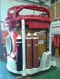 Side view of a closed bell showing the side hatch and cylinders for emergency gas supply of heliox and oxygen.