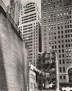 Old tenements with laundry from clotheslines are contrasted with imposing new skyscrapers