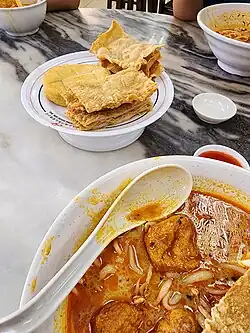 Image 129A bowl of curry mee, with fried beancurd skins and fish cake on the side (from Malaysian cuisine)