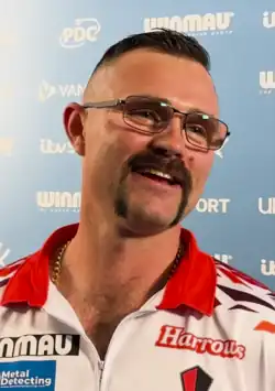 Damon Heta being interviewed at the 2025 PDC World Masters, standing in front of a panel with logos