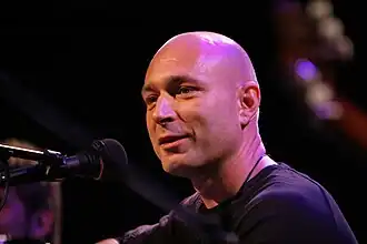 close-up of Daniel Landa in front of a microphone, looking left of camera with slight smile