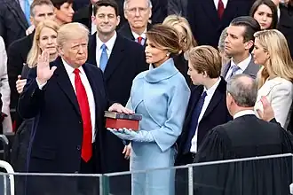 Trump, with his family watching, raises his right hand and places his left hand on the Bible as he takes the oath of office. Roberts stands opposite him administering the oath