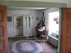 Room with oval braided rug on wood floor, door in opposite wall, small organ in corner, window at right