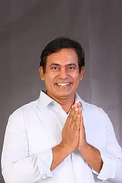 head-and-shoulders image of a dark-haired man smiling, with hands clasped as if in prayer