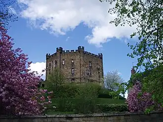 A stone three-story building with small windows on a grassy hill