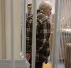 A slouching Lykov in a courtroom with handcuffs, facing away from the camera