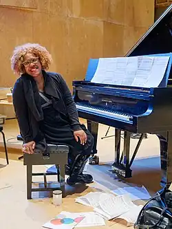 Wallen on a chair, leaning to look towards the camera, at a piano