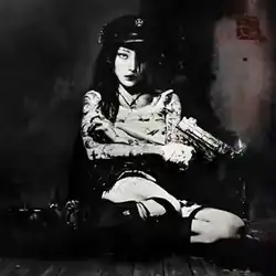 A person sitting with their legs sideways in the middle of the frame. A gun is in their hand, with a small flame coming out of it. The image is black and white.