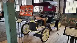 A green-colored, old-fashioned car with two seats and brass fittings