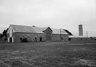A black and white picture of a long two story Quartermaster store building made of yellowish cut stone with a wooden second floor. The building is in the style of the late 1860s.