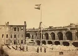1861 photograph of the interior of a damaged military fortification. The flag of the Confederate States of America flies from a flagpole near the center of the photograph.