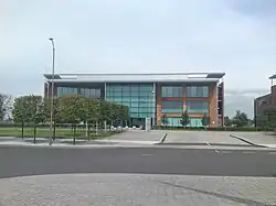 A wide orange rectangular building with turquoise windows, partly obscured on the left by rows of trees and a road light