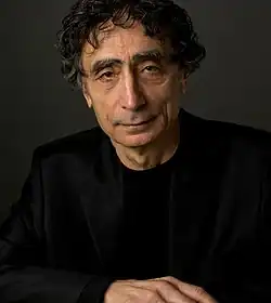 close-up of Gabor Maté wearing a black jacket, looking directly at the camera