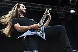 Close-up of Christian Andreu, long hair flying, playing a guitar with a cutaway bottom