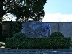 Vertical grey granite stone inscribed with Lüthi's name, surrounded by green hedges