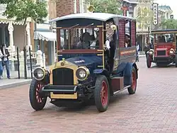 Two blue and red turn-of-the-20th-century-style cars on a brick road