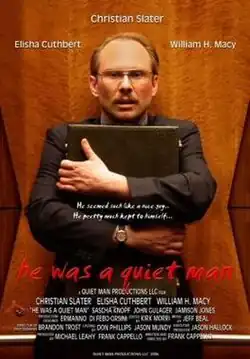 A man clutches a briefcase to his chase. He is against a wood panelled wall, he is wearing a brown suit, he has brown receding hair, a moustache, and wears glasses.