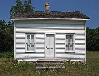 Tiny gabled house with clapboard siding and two windows flanking a central door