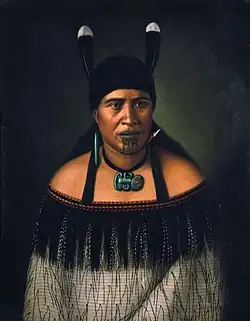 Image 44Hinepare of Ngāti Kahungunu, is wearing a traditional korowai cloak adorned with a black fringe border. The two huia feathers in her hair, indicate a chiefly lineage. She also wears a pounamu hei-tiki and earring, as well as a shark tooth (mako) earring. The moko-kauae (chin-tattoo) is often based on one's role in the iwi. (from Culture of New Zealand)