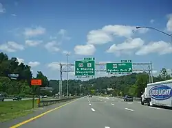 An asphalt highway heading toward some wooded hills.