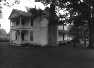 A black and white image of the James Dickson house, an early 19th century two story farm house with a pitched roof and front porch.
