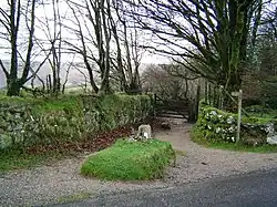 An earthen lane circles a raised grassy area containing a large stone