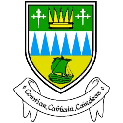 The logo of Kerrycoco as a flat badge with three levels; the bottom one yellow with a green ship, the middle white with blue spikes, and the top with green background with a crown