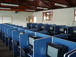 A computer lab, showing a number of desks containing CRT monitors, and the associated seating, with blue dividers in between individual workstations
