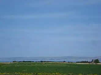 A green field stretches towards a distant body of water under a clear blue sky.
