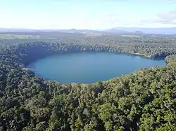 Aerial view of Lake Eacham, surrounded by dense tropical rainforest, with the agricultural land use of the Atherton Tablelnds in the background.