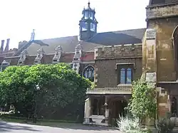 A long, low building of brick and stonework, with arched windows. It is partially obscured by trees and shrubs. The slate roof features a six-sided tower of stone and glass.