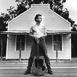 Larry Long standing with guitar in front of building