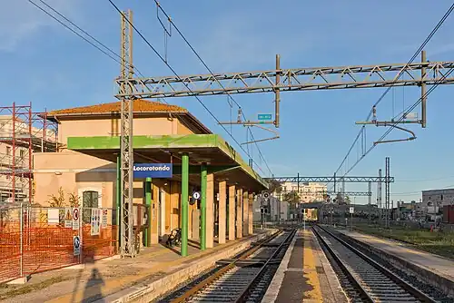 Two-story building with green canopy-covered platform next to two railway tracks