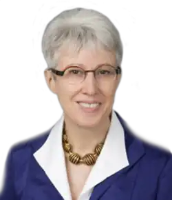 A photographic portrait of a middle-aged woman from the shoulders up, wearing a suit and eyeglasses