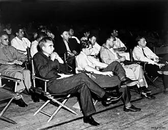 A group of men in shirtsleeves sitting on folding chairs